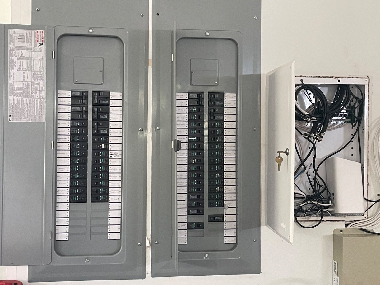 Two home electrical panels with the covers open for inspection, beside a low-voltage wiring box